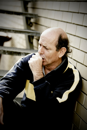 Man sitting against a brick wall coughing