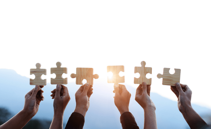 Conceptual image of 6 hands holding up puzzle pieces intended to represent each employee being an important piece of the puzzle.