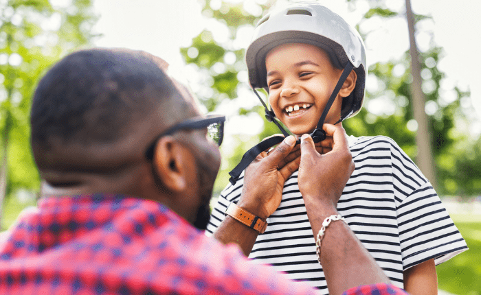 Father putting helmet on his male son.